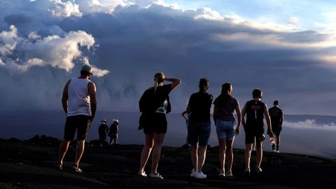 People stand on lava rock from a previous eruption near the Mauna Loa volcano as it erupts Wednesday near Hilo, Hawaii. 