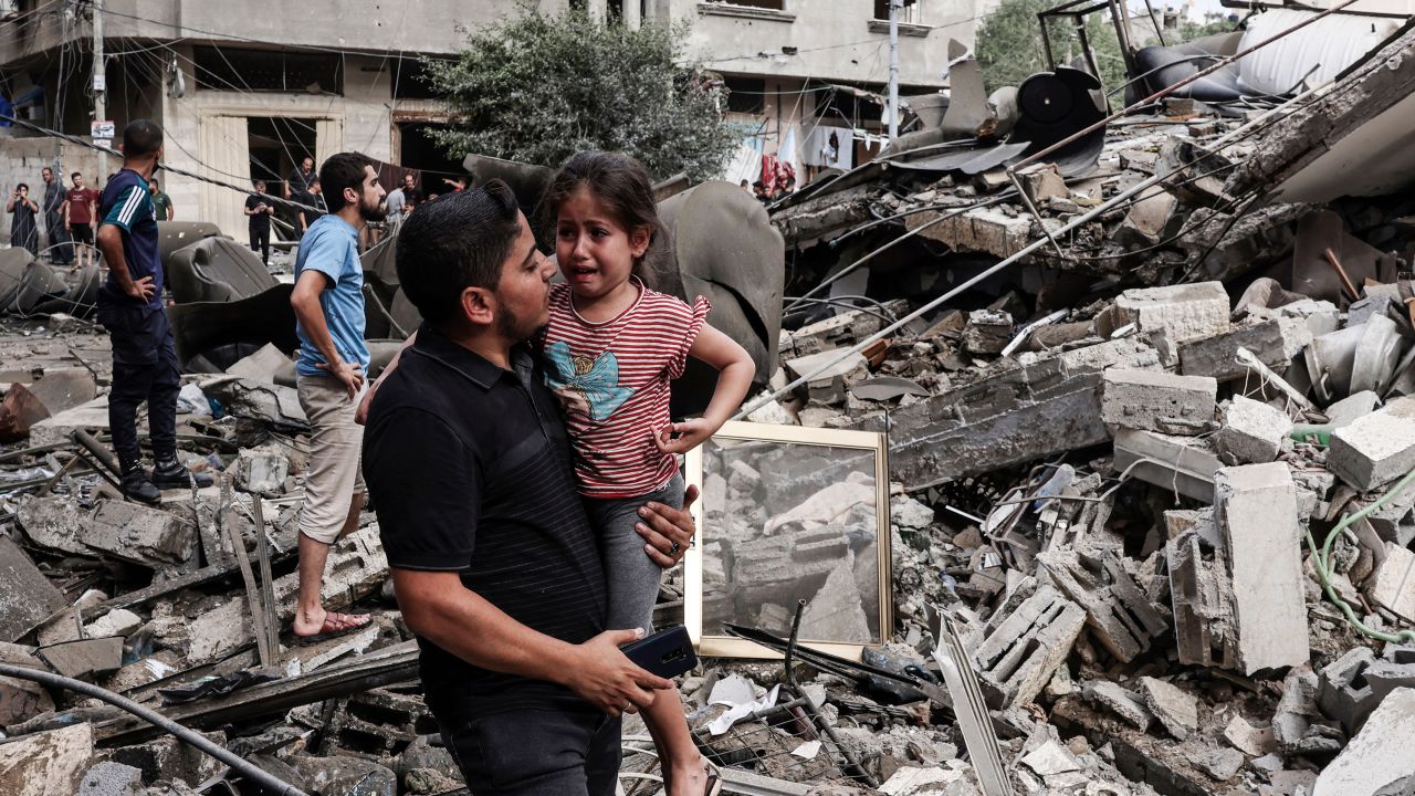 A man carries a crying child as he walks in front of a building destroyed in an Israeli air strike in Gaza City.