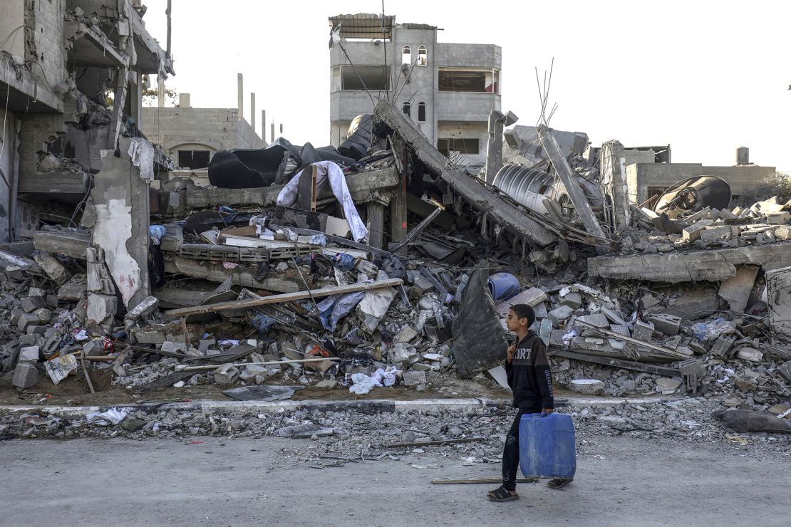 A Palestinian boy carrying water walks past a destroyed house in Rafah, October 18, 2023.
